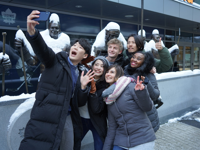 Internationale Sprachschüler machen ein Selfie vor verschneiten Skulpturen in Toronto