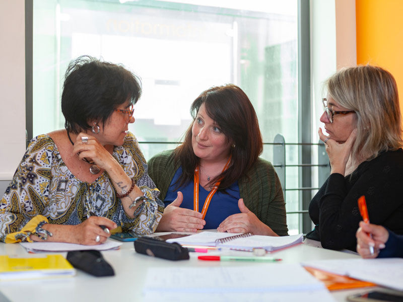 Lehrerin führt Gespräch mit zwei Teilnehmenden über Schreibtraining im Englischkurs