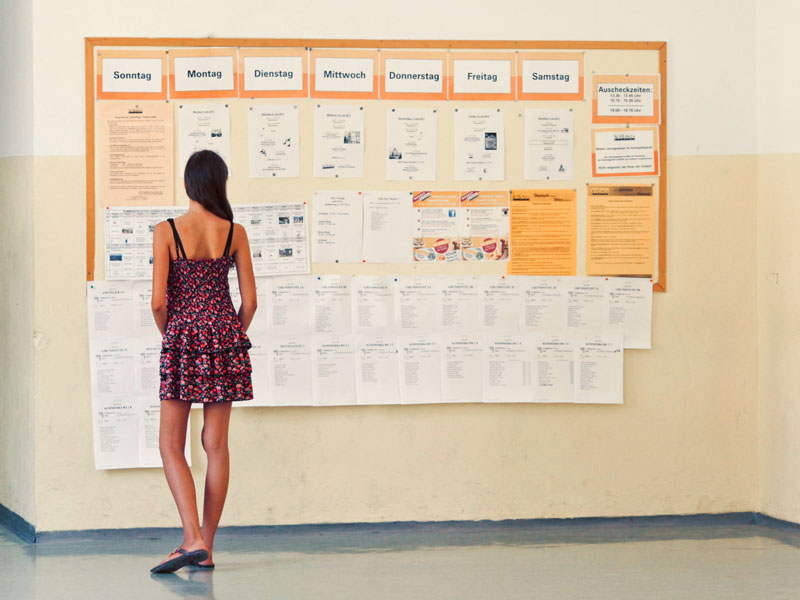 Schülerin betrachtet Aushänge und Wochenpläne an der Informationstafel der Schule