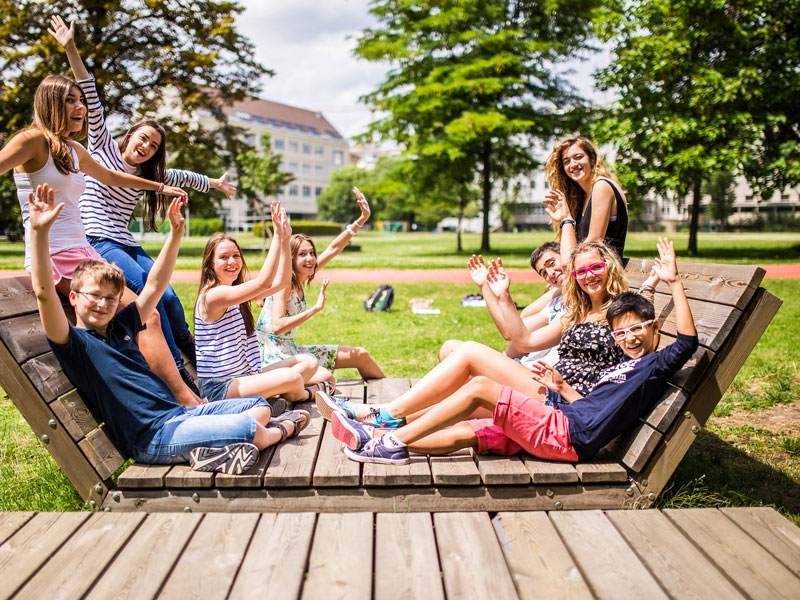 Gruppe junger Teilnehmender entspannt lachend im Park auf einer grossen Holzliege
