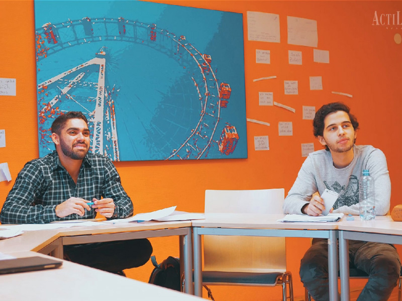 Kleingruppe beim Deutschunterricht in einem hellen Klassenraum mit oranger Wanddekoration