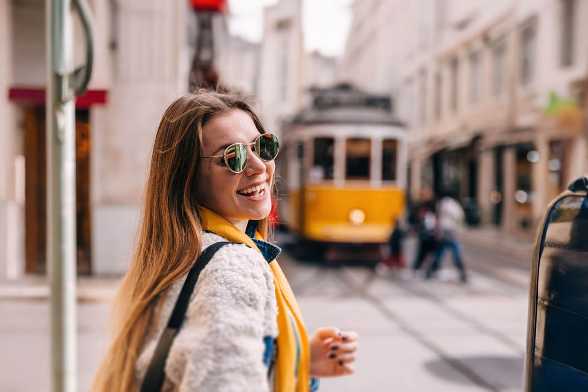 Lächelnde Person spaziert durch die Straßen Lissabons mit der gelben Straßenbahn im Hintergrund