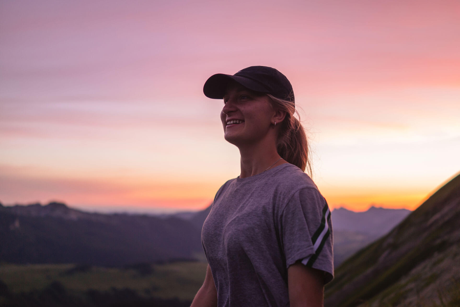 Lächelnde Person mit Kappe geniesst den Sonnenuntergang in den Schweizer Alpen