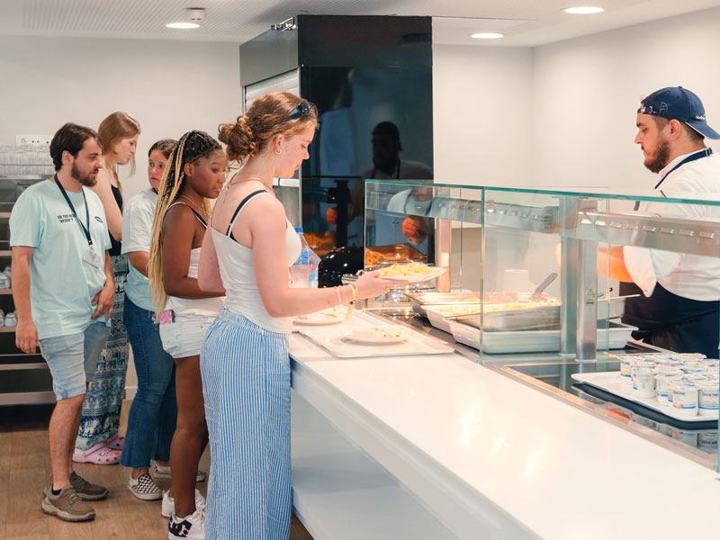 Schülerinnen und Schüler stehen in der Mensa der Sprachschule Expanish Barcelona an der Essensausgabe