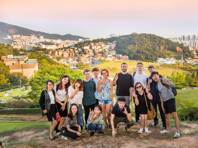 Gruppe internationaler Teilnehmender posiert mit Blick über die Hügel und Stadtlandschaft von Busan