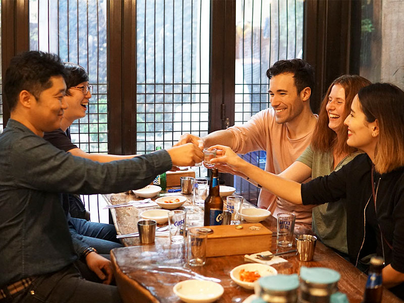 Gruppe von Teilnehmenden stößt bei einem gemeinsamen Abendessen in traditioneller Umgebung an