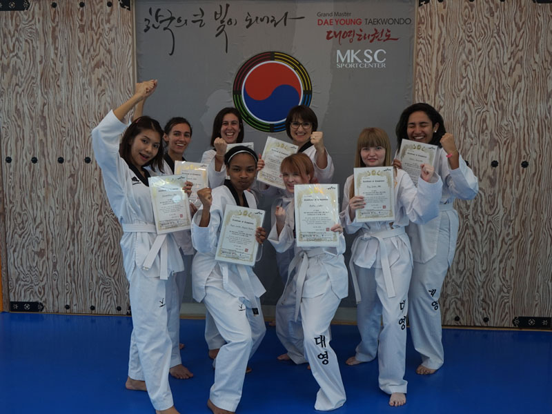 Gruppe in Taekwondo-Anzügen zeigt stolz ihre Urkunden nach dem Training