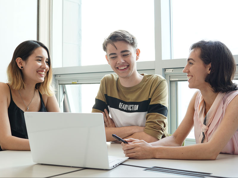 Drei Sprachschülerinnen und Sprachschüler arbeiten gemeinsam an einem Laptop im Unterrichtsraum