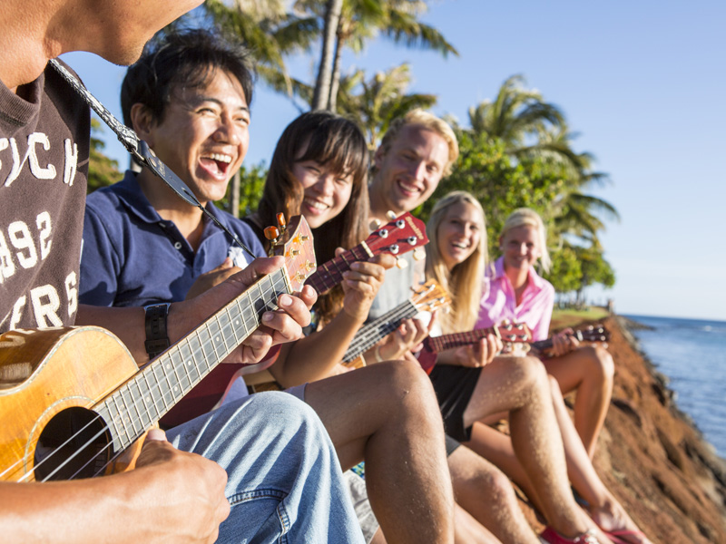Sprachschüler spielen Ukulele am Strand von Honolulu und genießen die Sonne Hawaiis