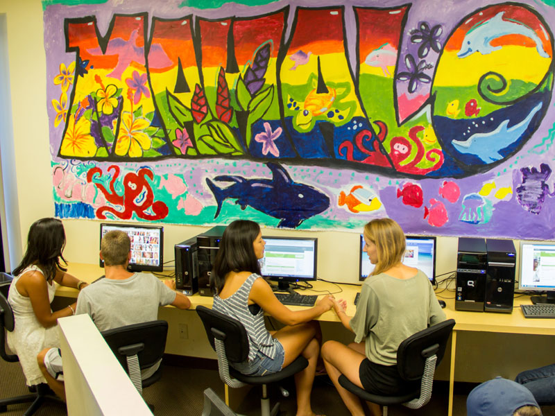 Computerraum der IIE Honolulu mit farbenfrohem Wandbild und Sprachschülern beim Lernen