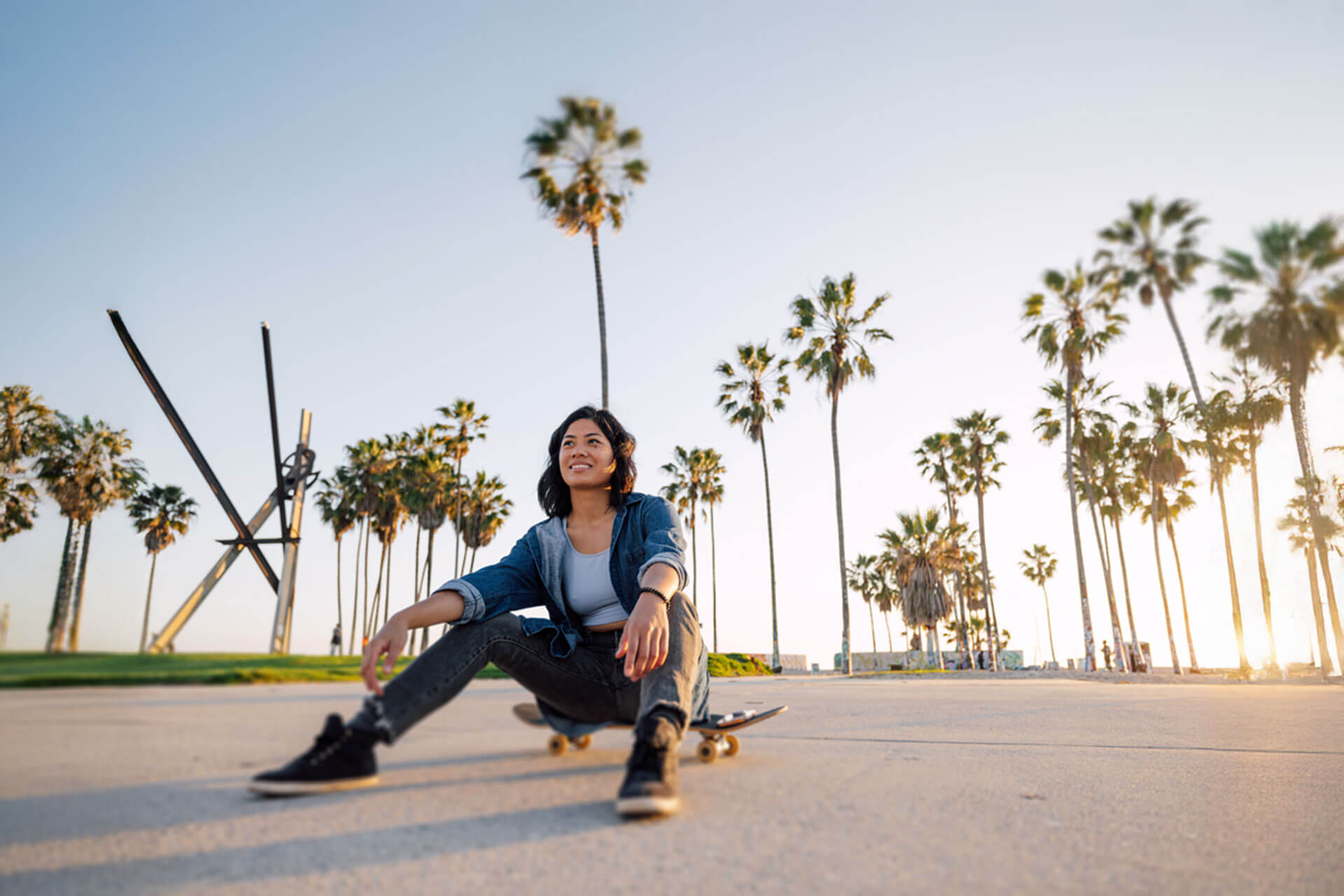 Junge Frau mit Skateboard am Venice Beach in Los Angeles bei Sonnenuntergang