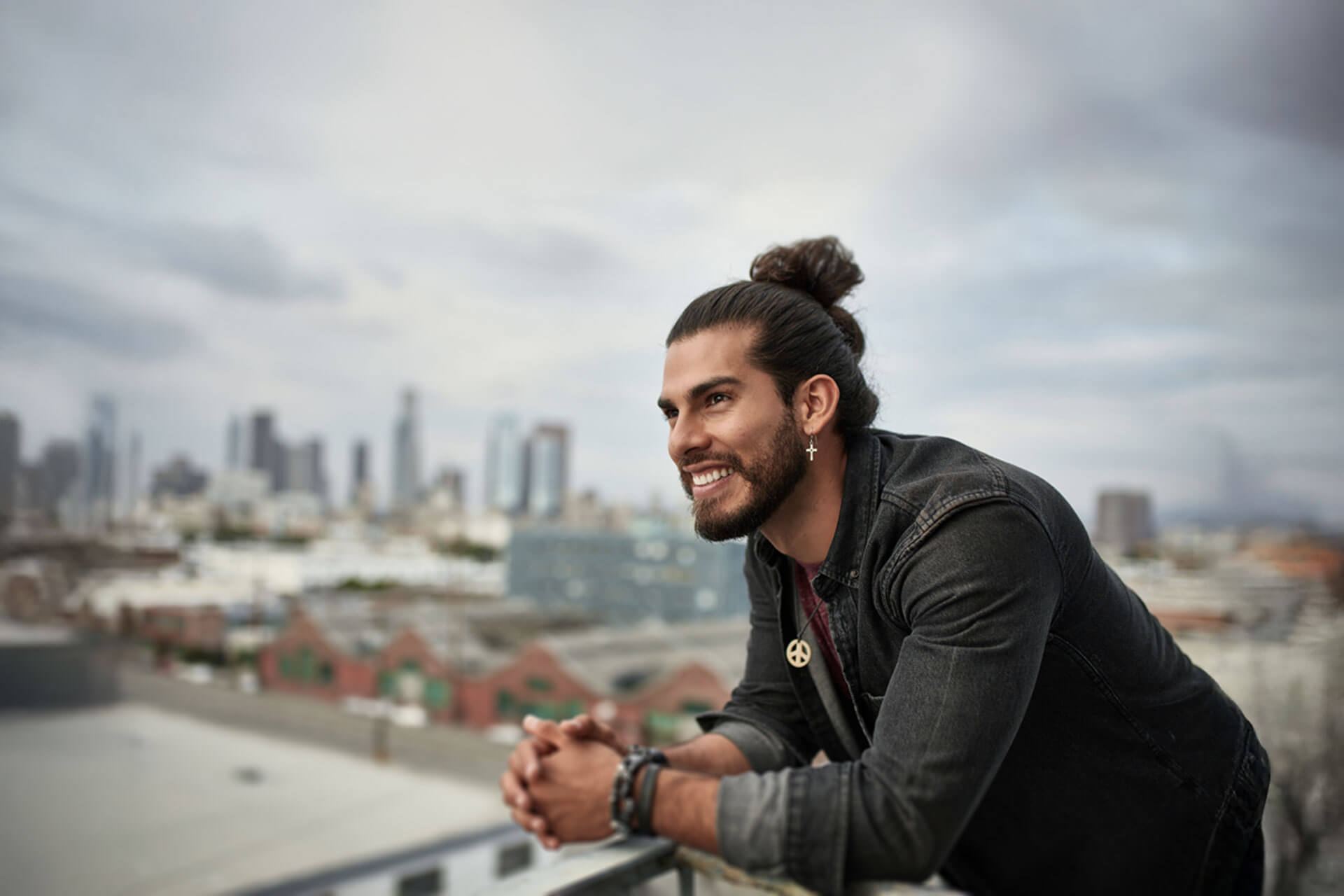 Junge Person auf Dachterrasse mit Blick auf die Skyline von Los Angeles bei bewölktem Himmel