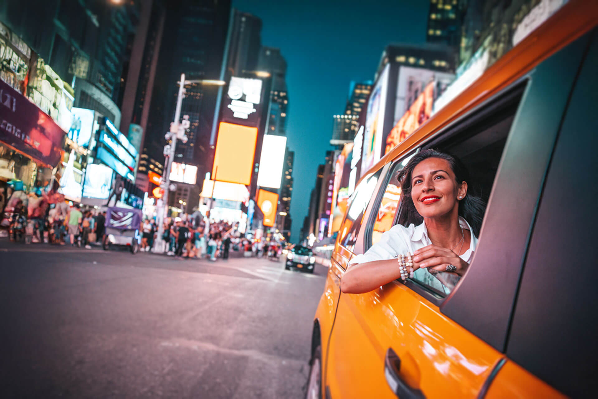 Frau lehnt sich aus dem Fenster eines gelben Taxis am Times Square in New York und blickt lächelnd auf die Lichter der Stadt