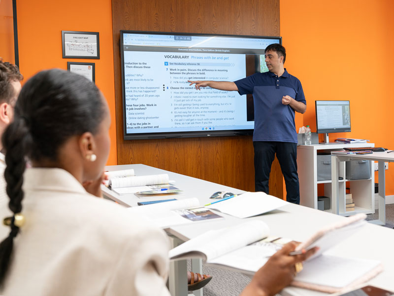 Lehrkraft erklärt Lerninhalte an Smartboard im modernen Klassenraum