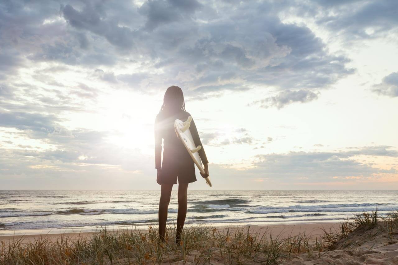 Surferin blickt auf die Brandung im Morgenlicht am Strand, Sprachkurs mit Aktivitäten am Meer.