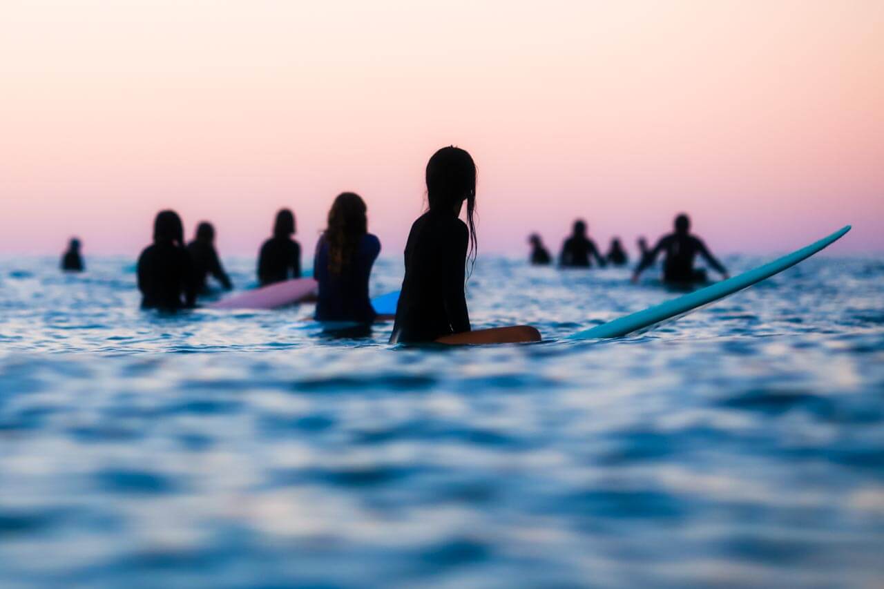 Surfergruppe sitzt im Wasser bei Dämmerung, Konversation üben über Hobbys nach dem Unterricht.