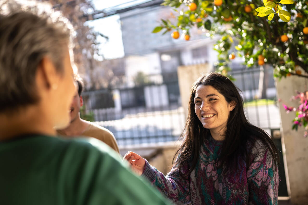 Lächelnde Frau begrüßt Freunde unter Orangenbaum in chilenischem Hof.