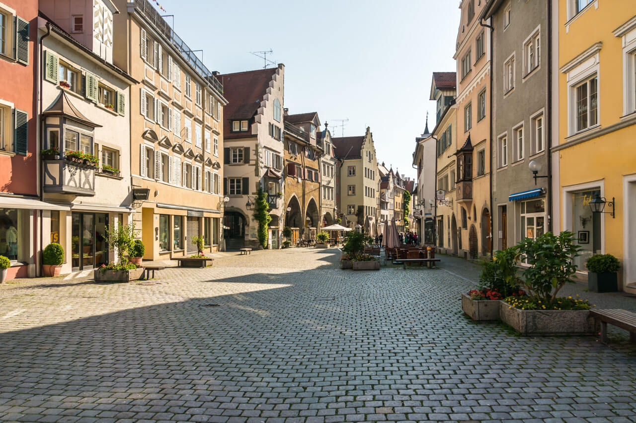 Pflasterplatz mit historischen Häuserzeilen, Arkaden und Cafés in einer ruhigen Gasse