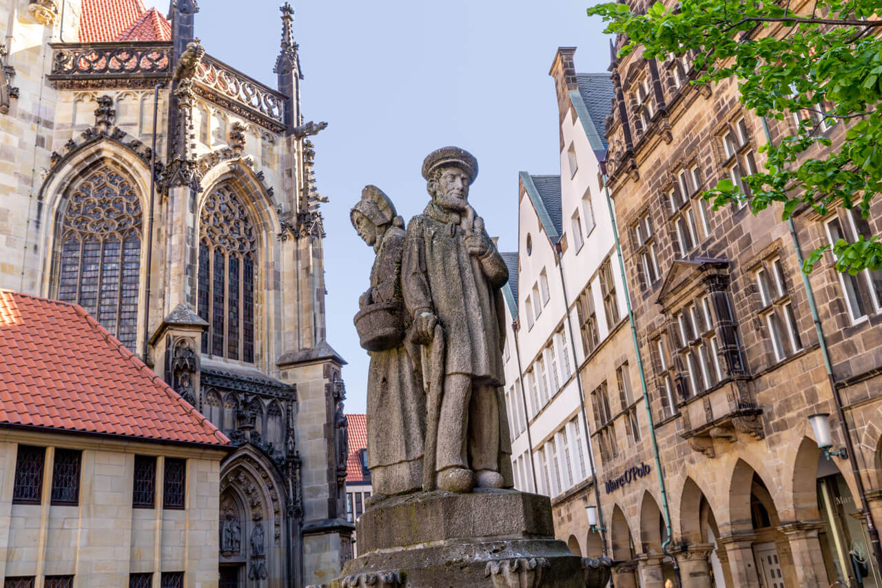 Statue des Kiepenkerl am Lambertikirchplatz vor den gotischen Fassaden der Lambertikirche.