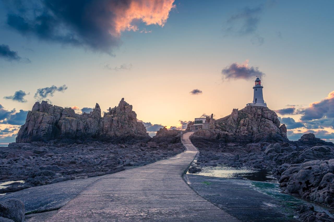 Leuchtturm La Corbière auf Jersey bei Sonnenuntergang über Felsen und Ebbeweg. Beliebtes Ausflugsziel für Lernende, Grammatik im Kopf, Natur vor Augen.