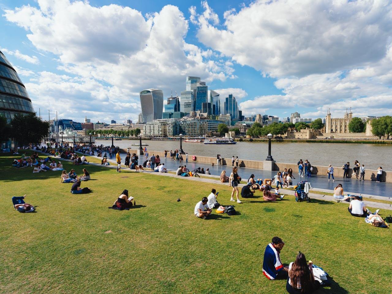 Menschen relaxen auf der Wiese an der South Bank mit Blick auf die Skyline der City of London Hörverstehen und Aussprache im Freien üben