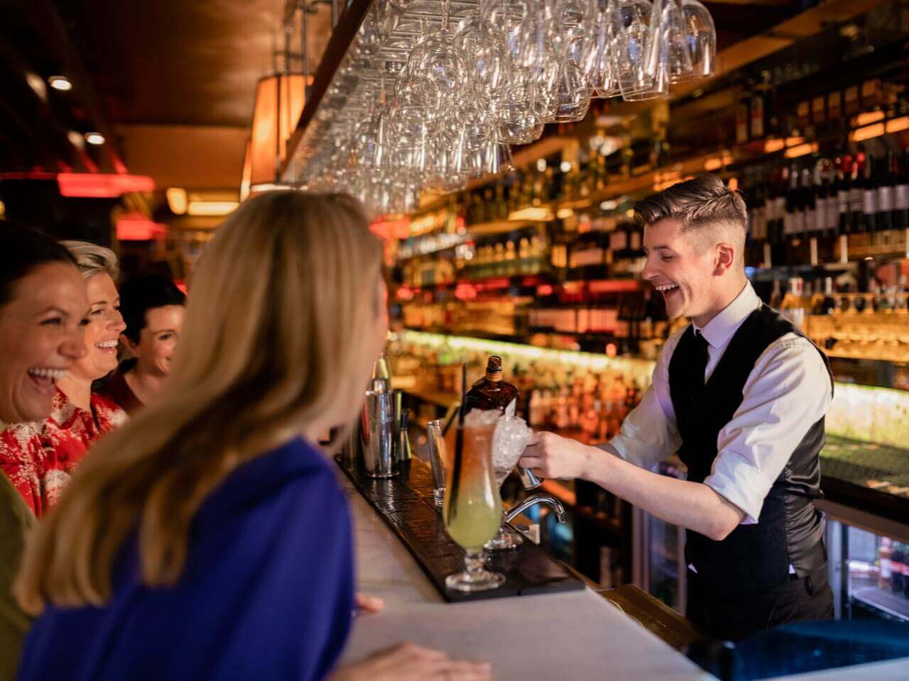 Barkeeper serviert Getränk für lachende junge Menschen in einer Bar in Newcastle Konversation üben im Pub nach dem Sprachkurs