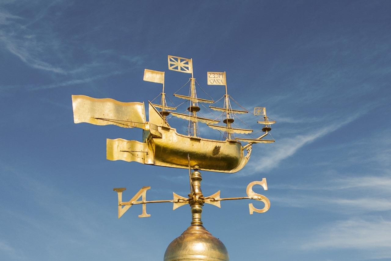 Goldene Schiffs-Wetterfahne vor blauem Himmel Aussprache von Himmelsrichtungen und Wettervokabeln üben