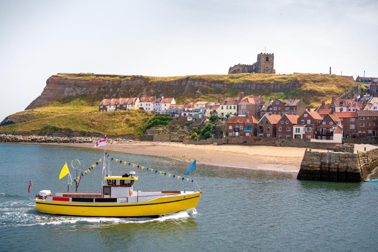 Küste von Whitby mit gelbem Ausflugsboot und roten Dächern Vokabeln zum Thema Meer anwenden beim Gespräch im Hafen