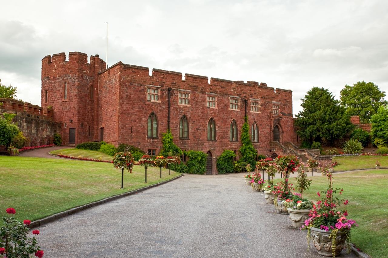Shrewsbury Castle aus rotem Sandstein mit Blumenschmuck entlang der Auffahrt Vokabeln zu Geschichte und Architektur anwenden im Englischkurs