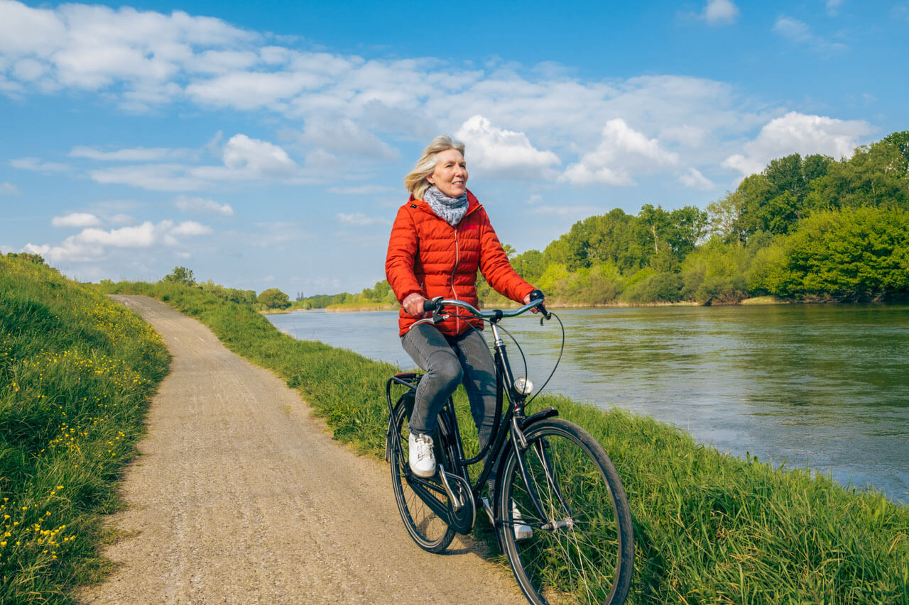 Frau fährt mit dem Rad am Fluss entlang Hörverstehen trainieren auf Sprachreise