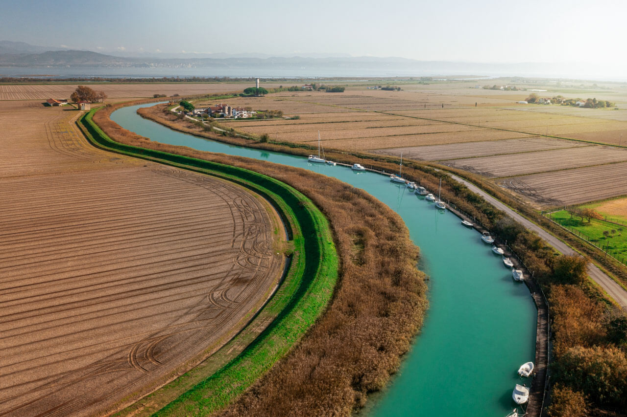 Wasserkanal bei Lignano mit Booten und Feldern – Naturkulisse für Sprachkurs Italienisch