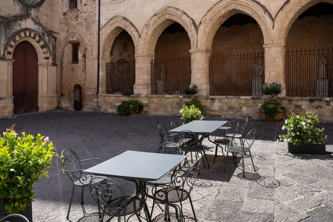 Kleiner Platz mit Tischen und Stühlen vor historischen Bögen in Tropea, Sprachreise Italienisch