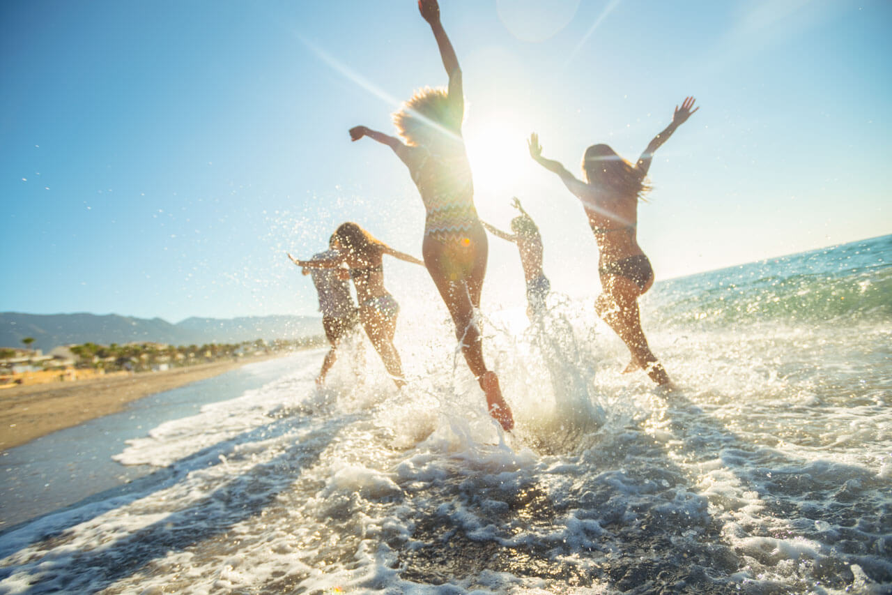 Gruppe junger Menschen springt lachend in die Wellen, Italienisch lernen kombiniert mit Freizeit.
