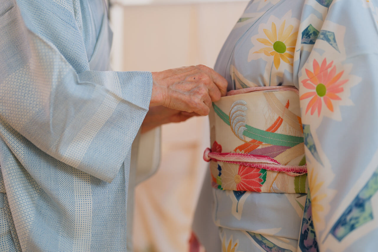 Nahaufnahme von Händen die den Obi an einem hellblauen Kimono binden