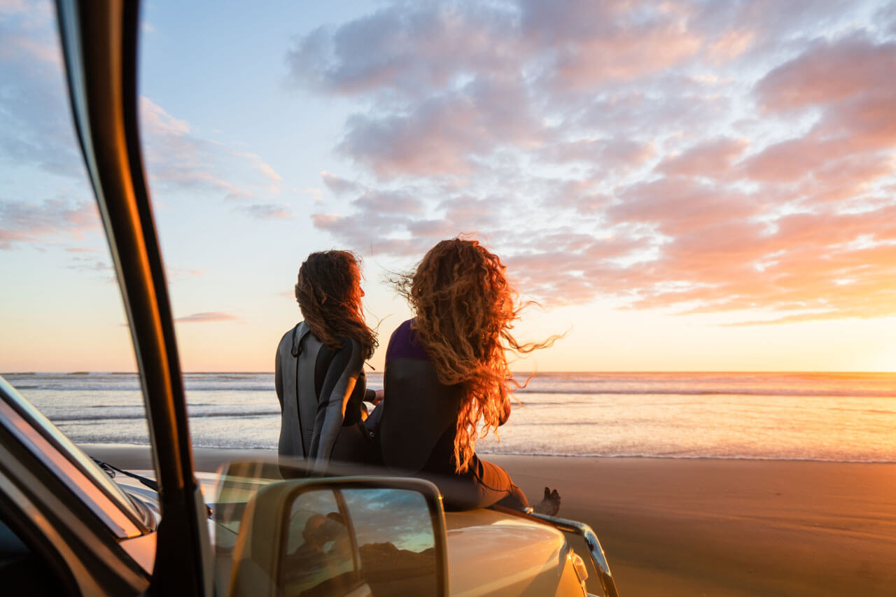 Zwei Personen am Strand bei Sonnenuntergang auf dem Auto, Pause vom Sprachkurs an der Küste.