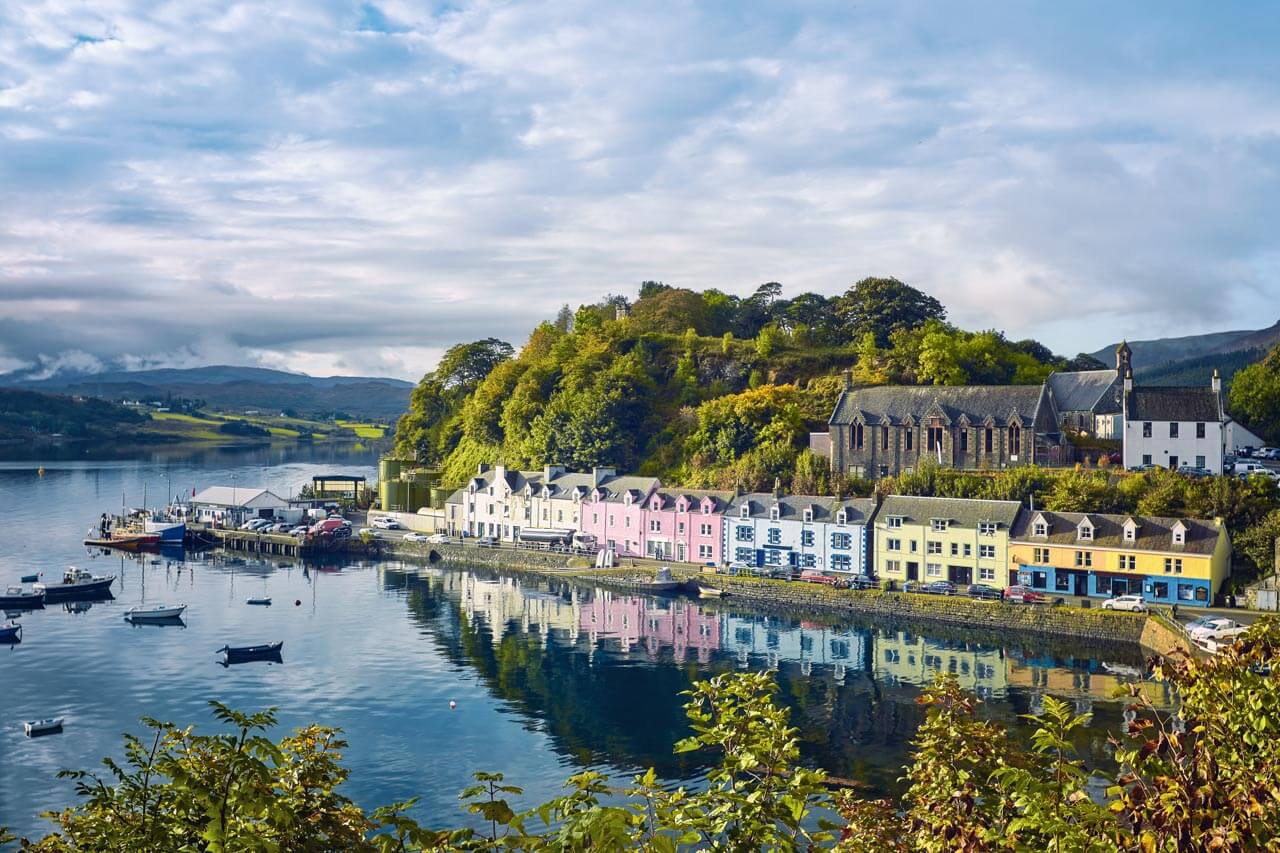 Bunte Häuserzeile am Hafen von Portree spiegelt sich im Wasser. Hörverstehen trainieren bei der Stadtführung.