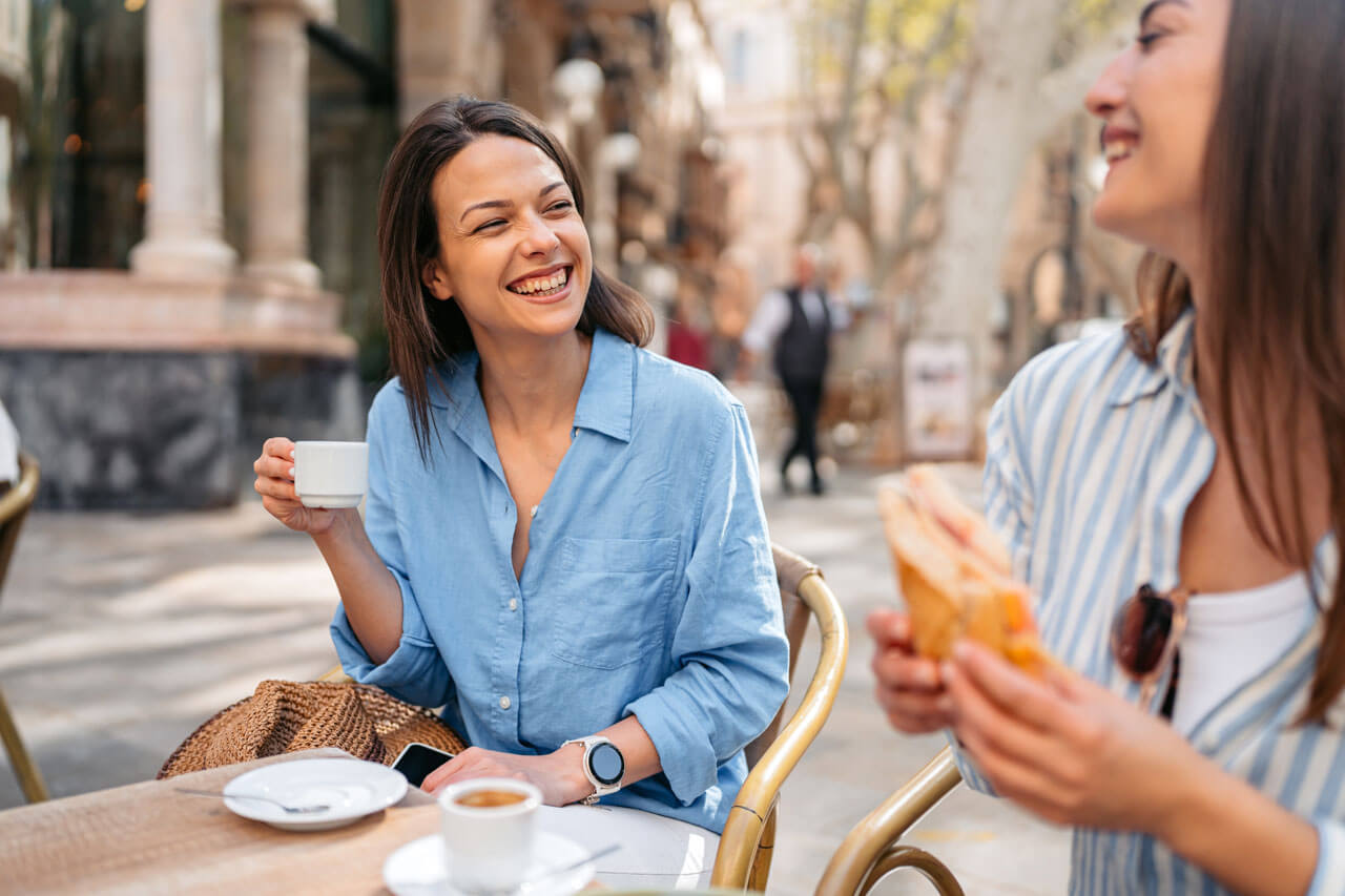 Zwei Freundinnen lachen bei Kaffee auf einer Straßenterrasse in Palma.