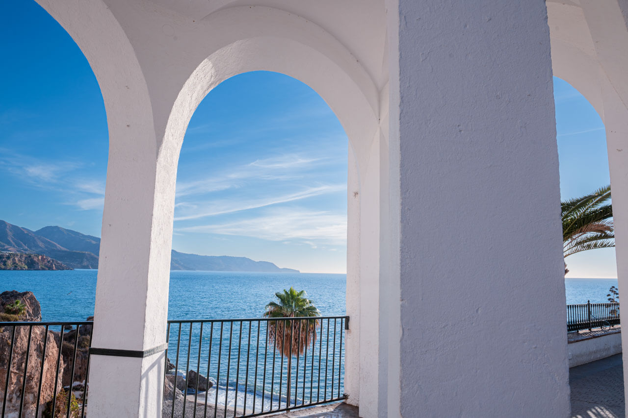 Blick durch die weißen Bögen des Balcón de Europa auf das Mittelmeer und eine Palme