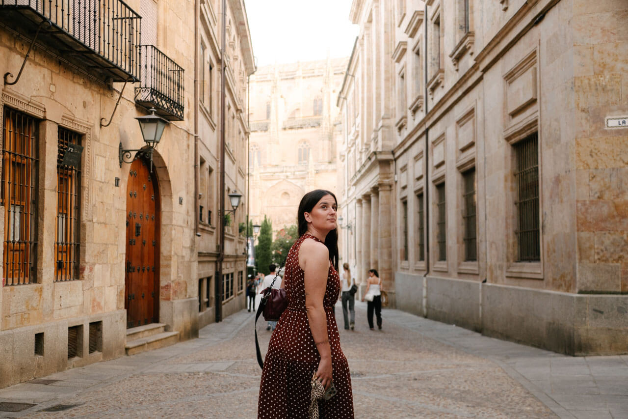 Frau schlendert durch die sandsteinfarbenen Gassen der Altstadt von Salamanca, im Hintergrund die Kathedrale.