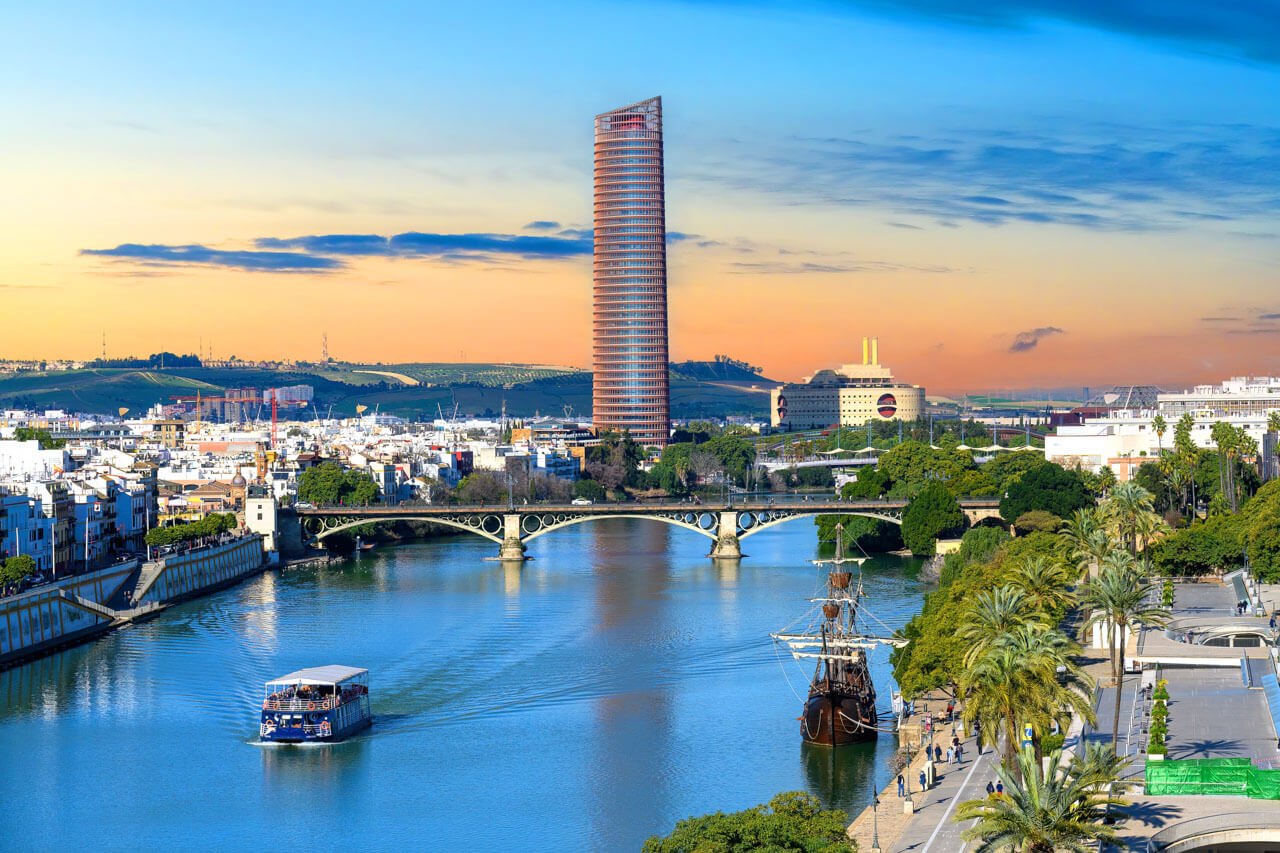 Guadalquivir bei Sonnenuntergang mit Torre Sevilla, Bogenbrücke und Ausflugsschiff.