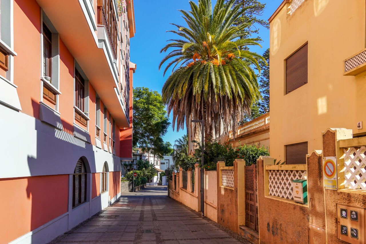 Sonnige Gasse in San Cristóbal de La Laguna mit Pastellfassaden, Palmen und ruhigem Fußweg.