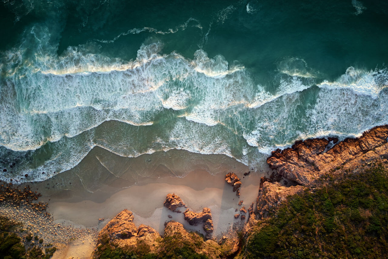 Drohnenaufnahme von Wellen an felsiger Küste, Schreibtraining zu Naturthemen.