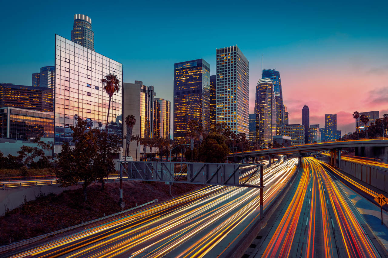 Skyline bei Sonnenuntergang mit Lichtspuren auf dem Freeway. Business Englisch und Hörverstehen im Kontext üben.