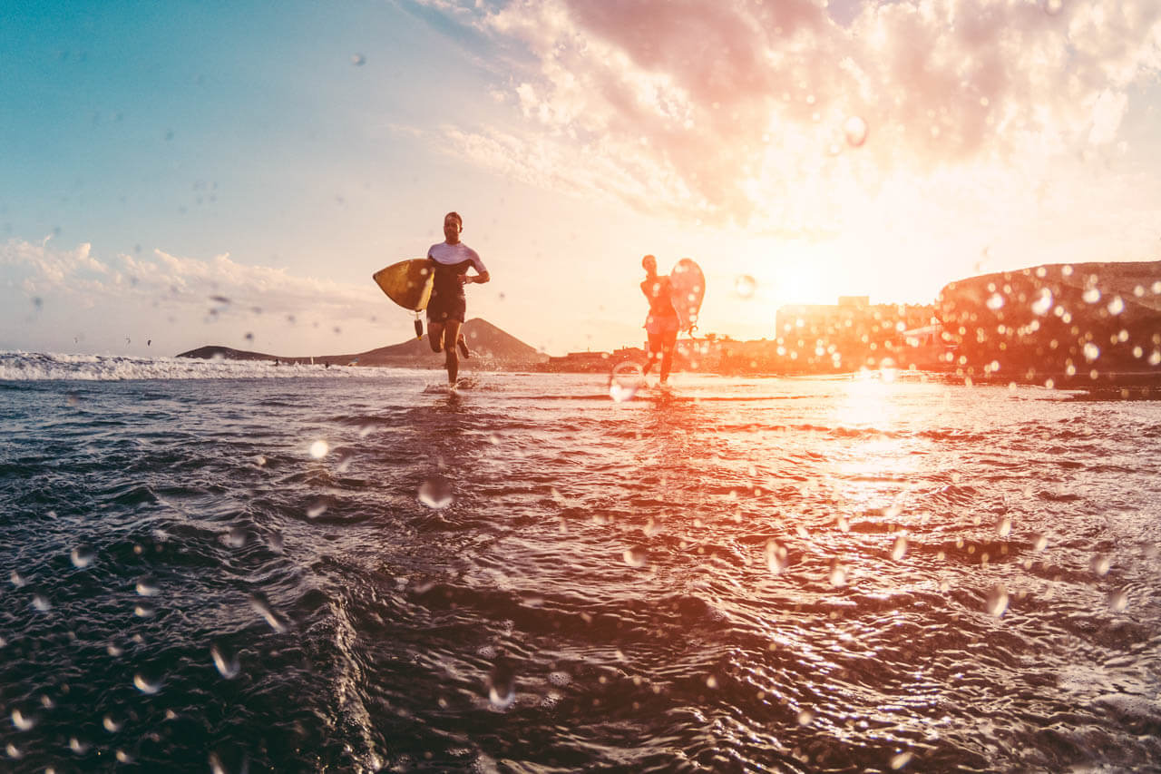 Surfer laufen ins Wasser bei Sonnenaufgang. Sprachkurs am Meer, Lernen in der Gruppe und Exkursion.