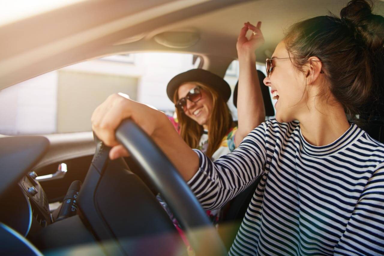 Zwei Reisende singen im Auto auf Roadtrip, Konversation üben im realen Alltag.
