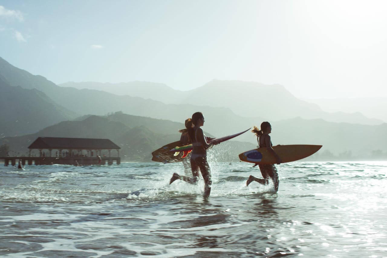 Gruppe mit Surfboards rennt ins Meer am Pier, Sprachreise Hawaii mit Lernen nach dem Unterricht.