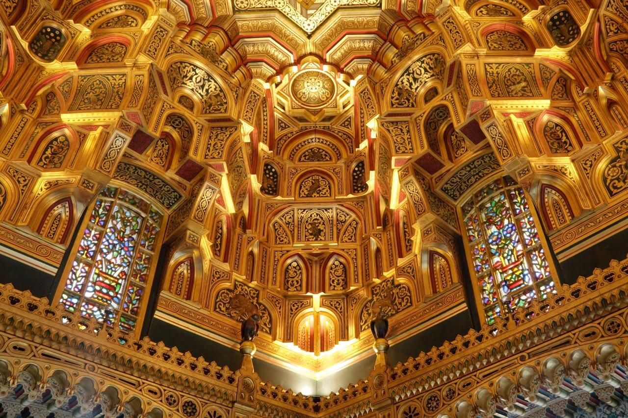 Vergoldetes Deckenornament mit Buntglasfenstern in einem Schloss. Grammatik trainieren im Kontext.