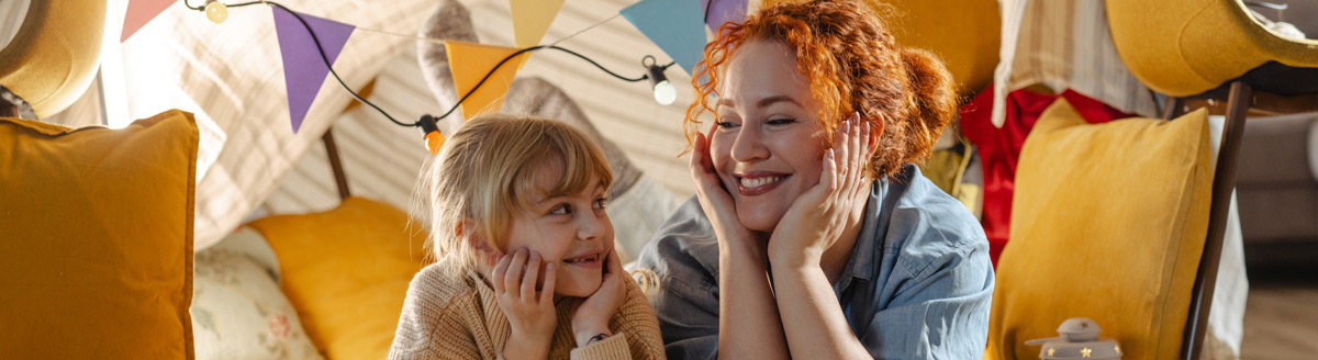 Junge Frau und Kind lachen gemeinsam in gemütlicher Umgebung bei einer Gastfamilie.