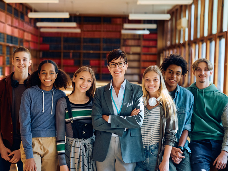 Schulklasse mit Lehrerin lächelt gemeinsam in einer Bibliothek im Ausland.
