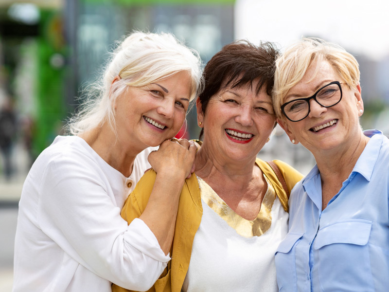 Drei Seniorinnen lächeln fröhlich bei einer Sprachreise im Ausland.